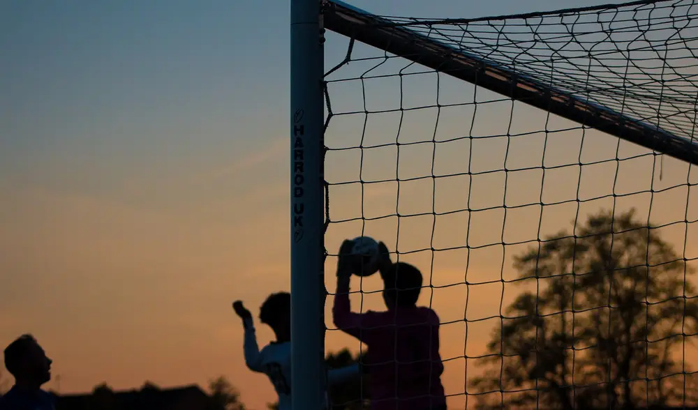 Silhueta de um guarda-redes a agarrar a bola ao fim da tarde, contra um céu claro