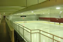 Pista de gelo de um pavilhão comunitário vista da galeria superior, com os bancos junto às tabelas