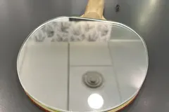 Raquete de ténis de mesa pousada sobre uma superfície clara, ao lado de uma bola