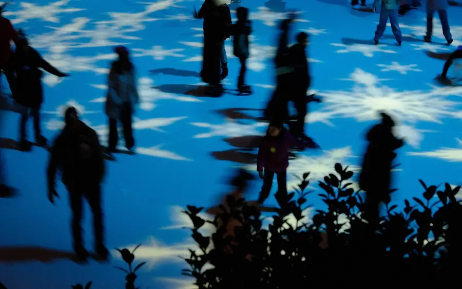 Pista de patinagem no gelo instalada numa praça urbana, delimitada por barreiras baixas