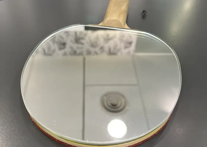 Raquete de ténis de mesa pousada sobre uma superfície clara, ao lado de uma bola